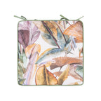 An outdoor chair pad with a tropical leaf print in muted earthy tones of green, orange, purple, and beige on a white background, finished with an green trim and ties.