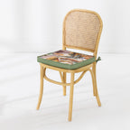 A light natural wood dining chair with a woven cane backrest, featuring a thick seat cushion with a multicolor leaf pattern and an green edge, set against a clean white background.