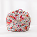 A bean bag chair with a tropical floral print featuring hibiscus flowers and palm leaves in pink, red, green, and orange on a light beige background, set against a plain white studio backdrop.