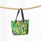 A beach bag with a green tropical leaf print and black handles, hanging from a thick natural rope against a plain white background.