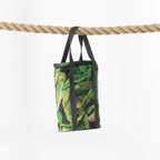 A cooler bag with a green tropical banana leaf pattern and black handles, hanging from a thick natural rope against a clean white background.