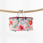 A rectangular folding cooler basket with a vibrant tropical floral print, suspended by a black handle from a thick natural rope against a clean white background.