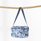 A blue and white tropical leaf print cooler bag with a blue strap, hanging from a thick natural rope against a clean white background.