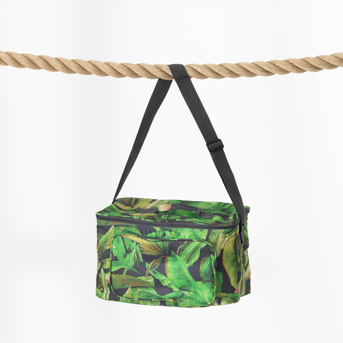 A green tropical leaf print cooler bag with black straps, hanging from a thick natural rope against a clean white background.