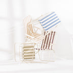 Four striped folding beach chairs in Green Stripe, Blue Stripe, Natural Stripe and Mocha stacked and arranged together on a white studio background.