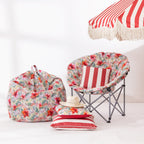 A coordinated outdoor furniture set displayed against a white wall, including a large floral bean bag chair, a folding moon chair with a red-and-white striped cushion, a matching striped pillow, a straw hat, and part of a red-and-white striped umbrella.