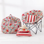 A coordinated outdoor furniture set displayed against a white wall, including a large floral bean bag chair, a folding moon chair with a red-and-white striped cushion, a matching striped pillow with a straw hat.