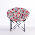 A folding moon chair with a curved, crescent-shaped seat upholstered in a vibrant tropical floral print, supported by a silver metal frame, shown on a white studio background.
