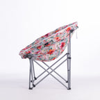 A folding moon chair with a curved, crescent-shaped seat upholstered in a vibrant tropical floral print, supported by a silver metal frame, shown on a white studio background.