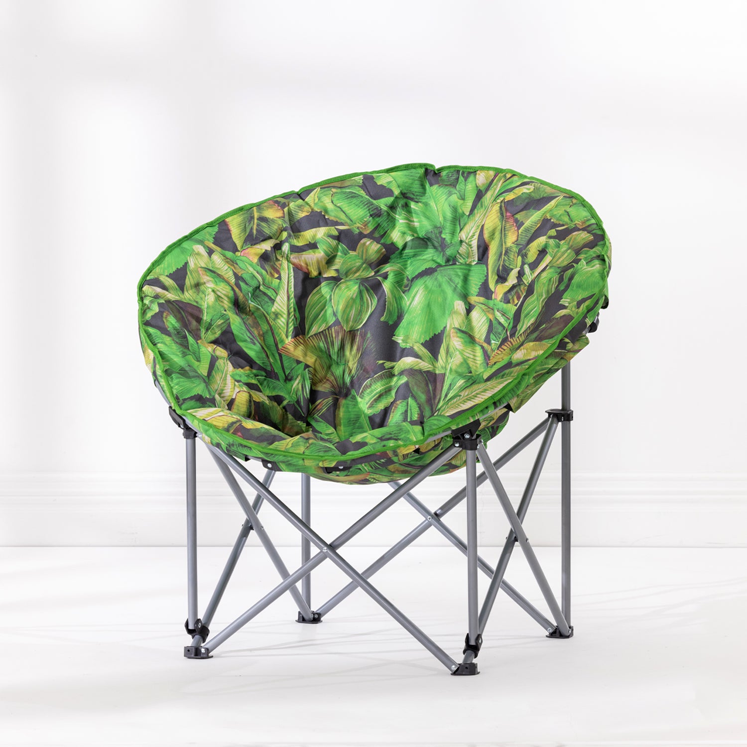 A round fabric moon lounge chair with a vibrant green tropical leaf print, supported by a silver metal folding frame, set against a clean white studio background.