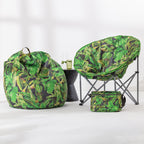 A coordinated outdoor seating set with a green tropical leaf print bean bag chair, a matching folding moon chair, and a small matching cooler bag, displayed on a clean white studio floor with a small dark side table between them.