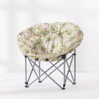 A folding moon chair with a round cushion upholstered in a palm tree pattern on a ivory background, supported by a silver metal frame.
