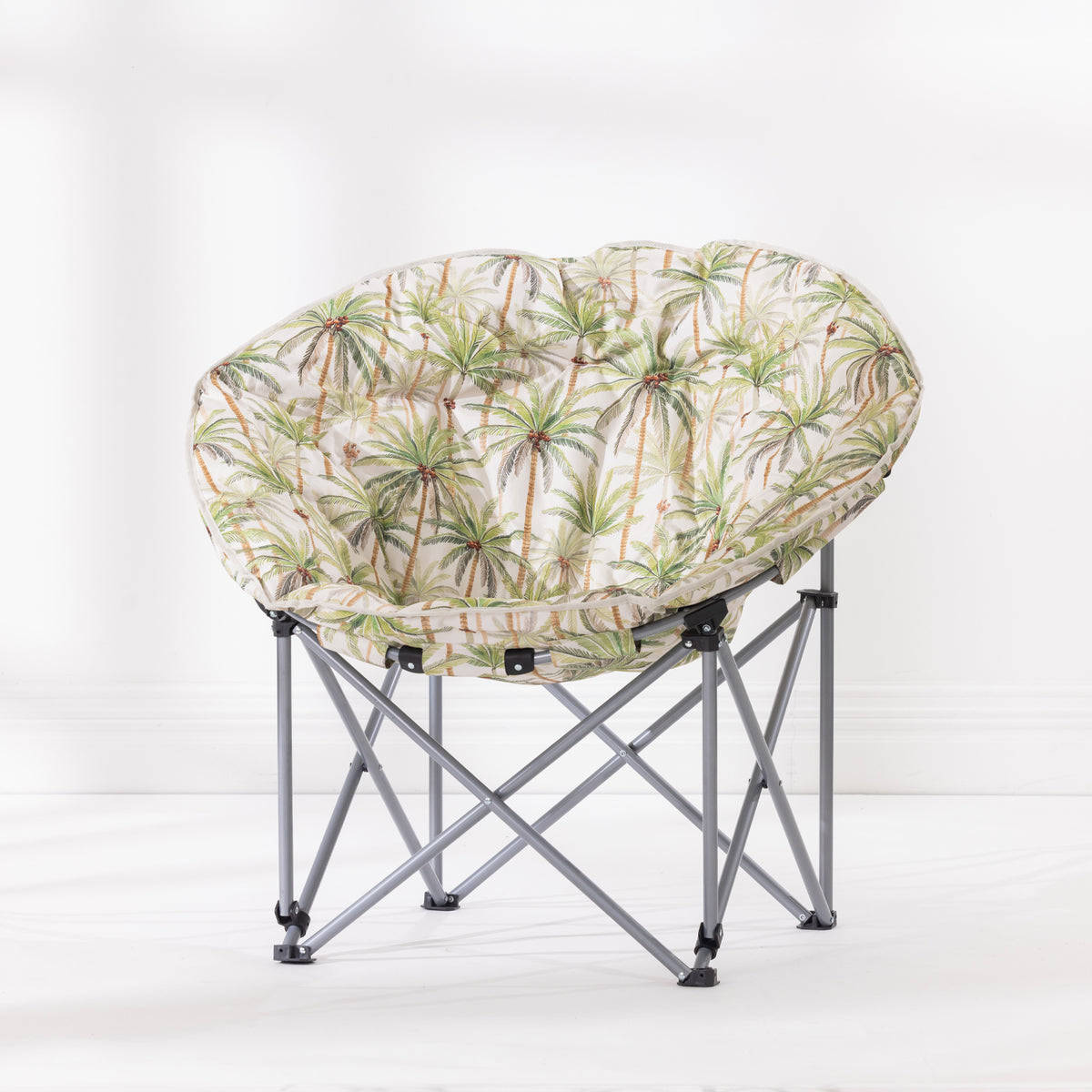 A folding moon chair with a round cushion upholstered in a palm tree pattern on a ivory background, supported by a silver metal frame.