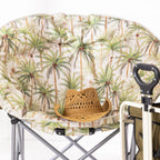 A close up of a round moon chair with a tropical palm tree print cushion, shown with a woven straw hat resting on the seat. 