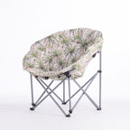 A folding moon chair with a ivory-colored fabric seat cushion featuring a green palm tree pattern, supported by a silver metal frame, shown against a plain white background.