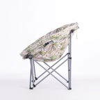 A folding moon chair with a ivory-colored fabric seat cushion featuring a green palm tree pattern, supported by a silver metal frame, shown against a plain white background.