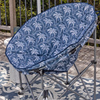 A blue and white palm tree patterned outdoor moon chair, set on a patterned rug on a wooden deck.