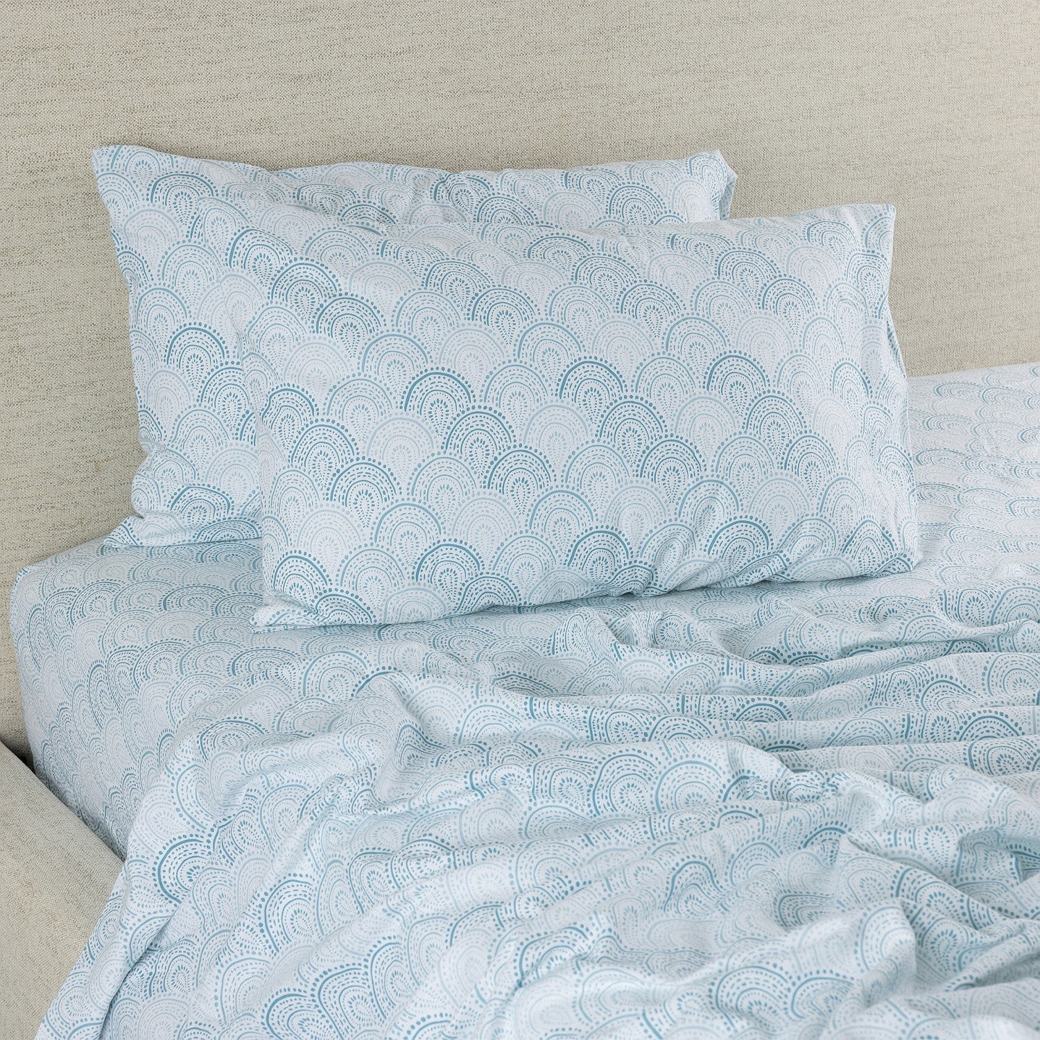 Blue patterned bedding set on a bed with a beige headboard.