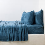 Blue textured sheet set and pillows on a beige sofa against a white wall