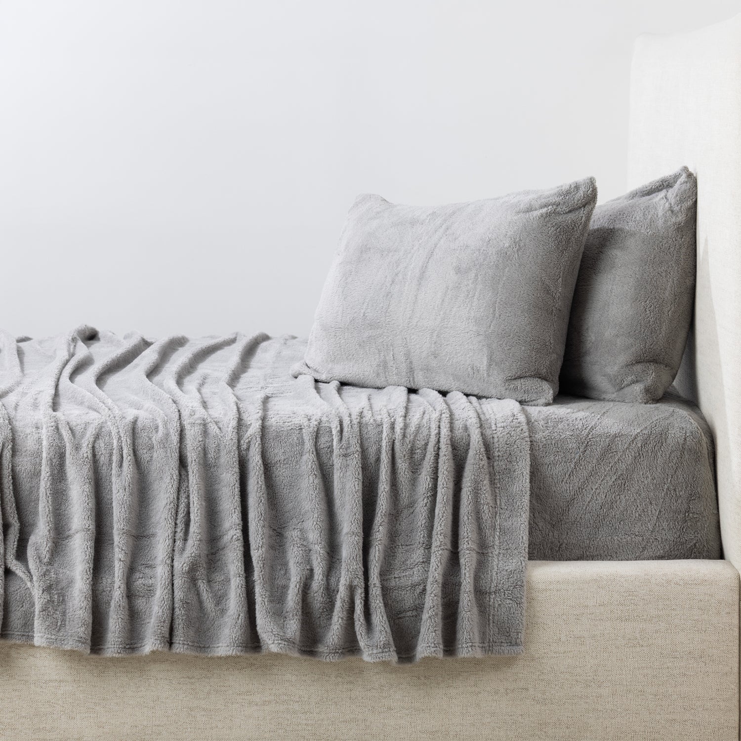 Gray bedding set on a bed with a white wall background