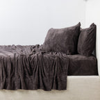Dark brown textured sheet set and pillows on a bed against a white wall