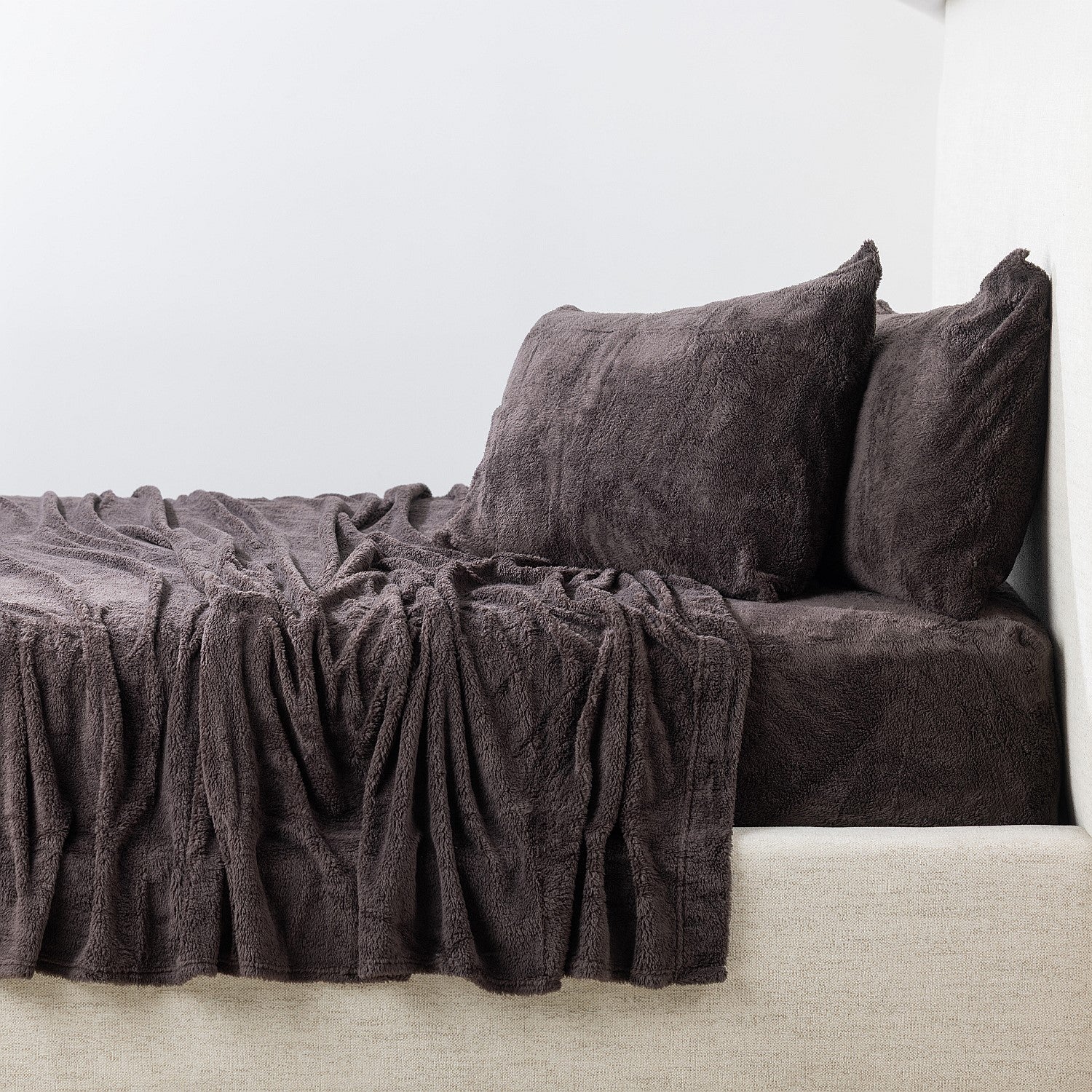 Dark brown textured sheet set and pillows on a bed against a white wall