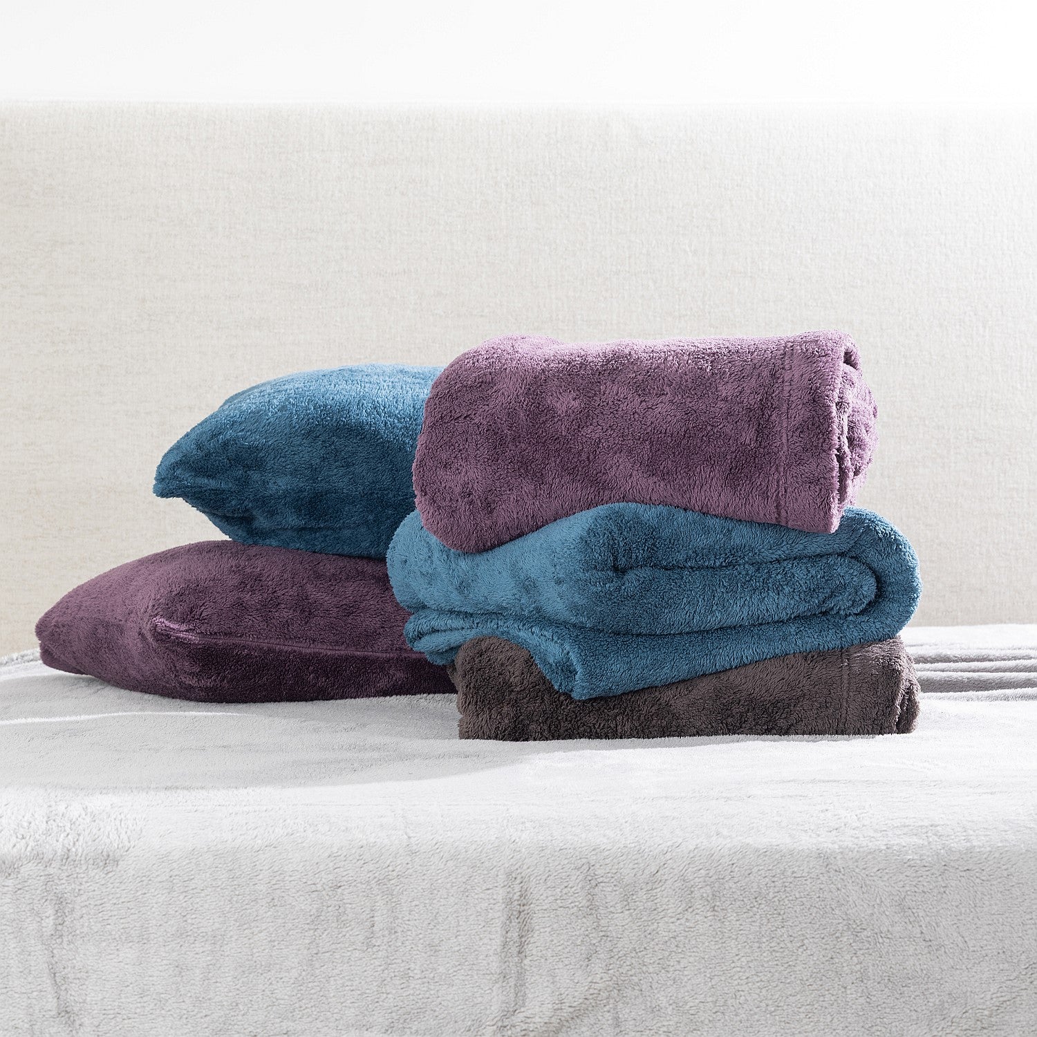 Stack of folded sheet sets in purple and blue on a bed with a neutral background