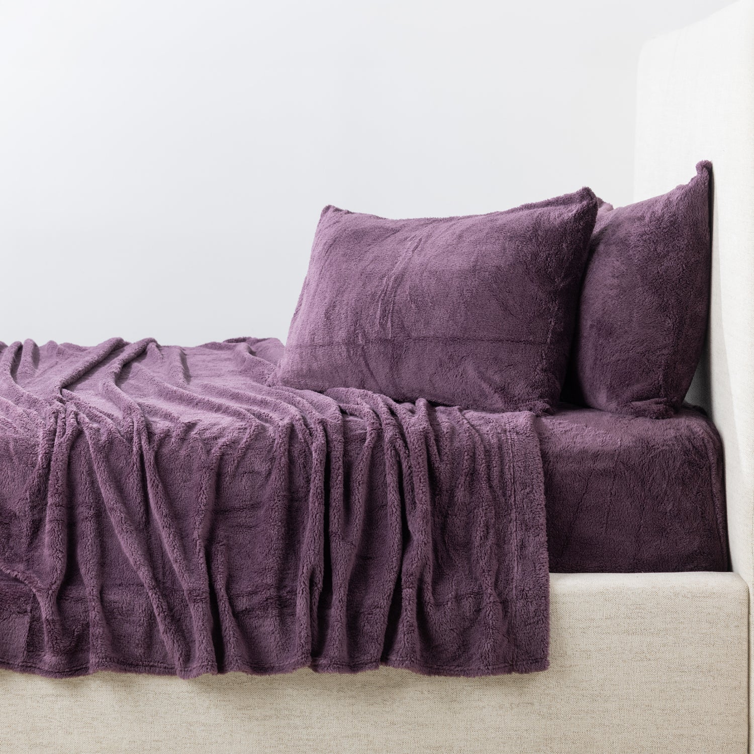 Purple textured sheets and pillows on a bed against a white wall.