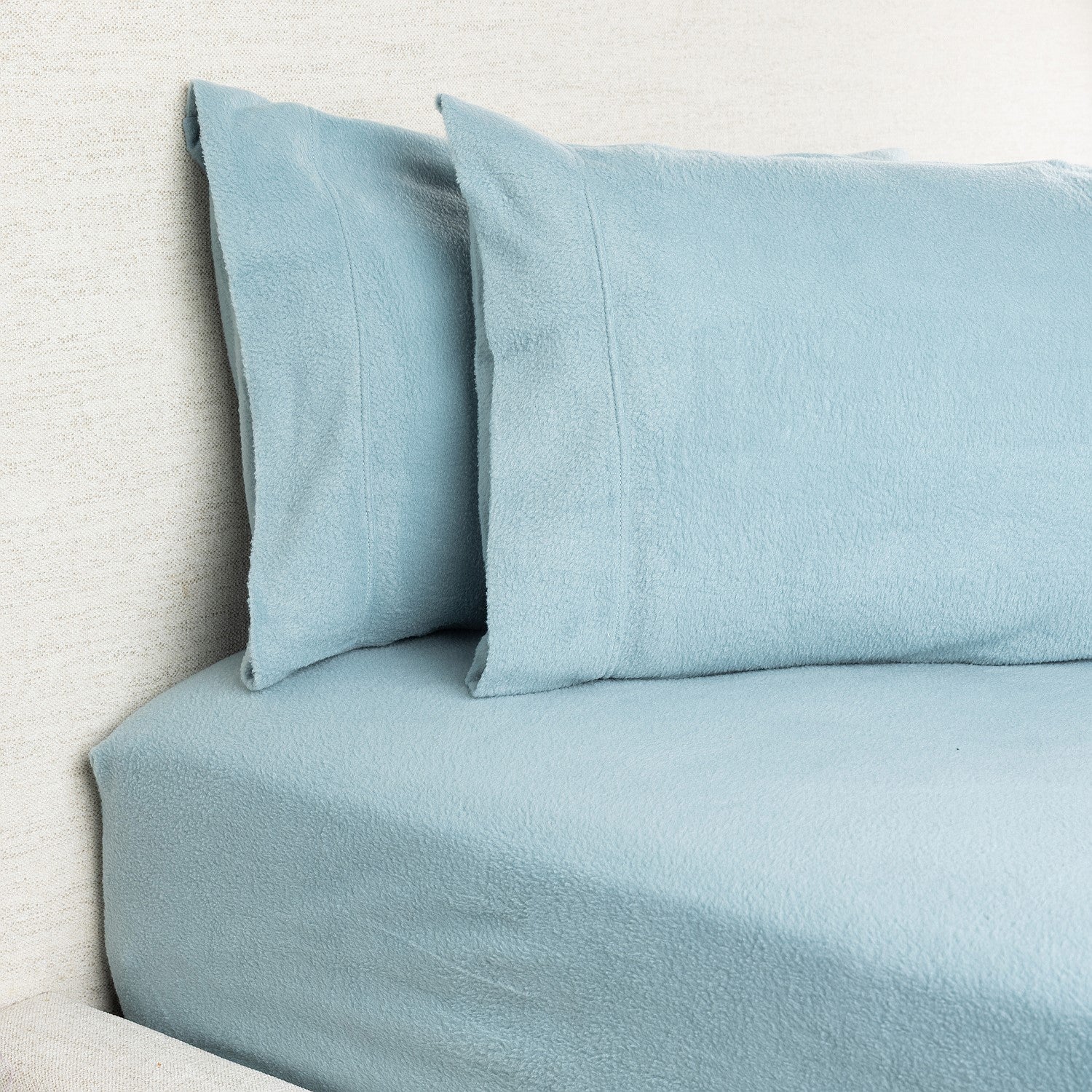 Light blue bedding set with pillows on a bed against a neutral wall.