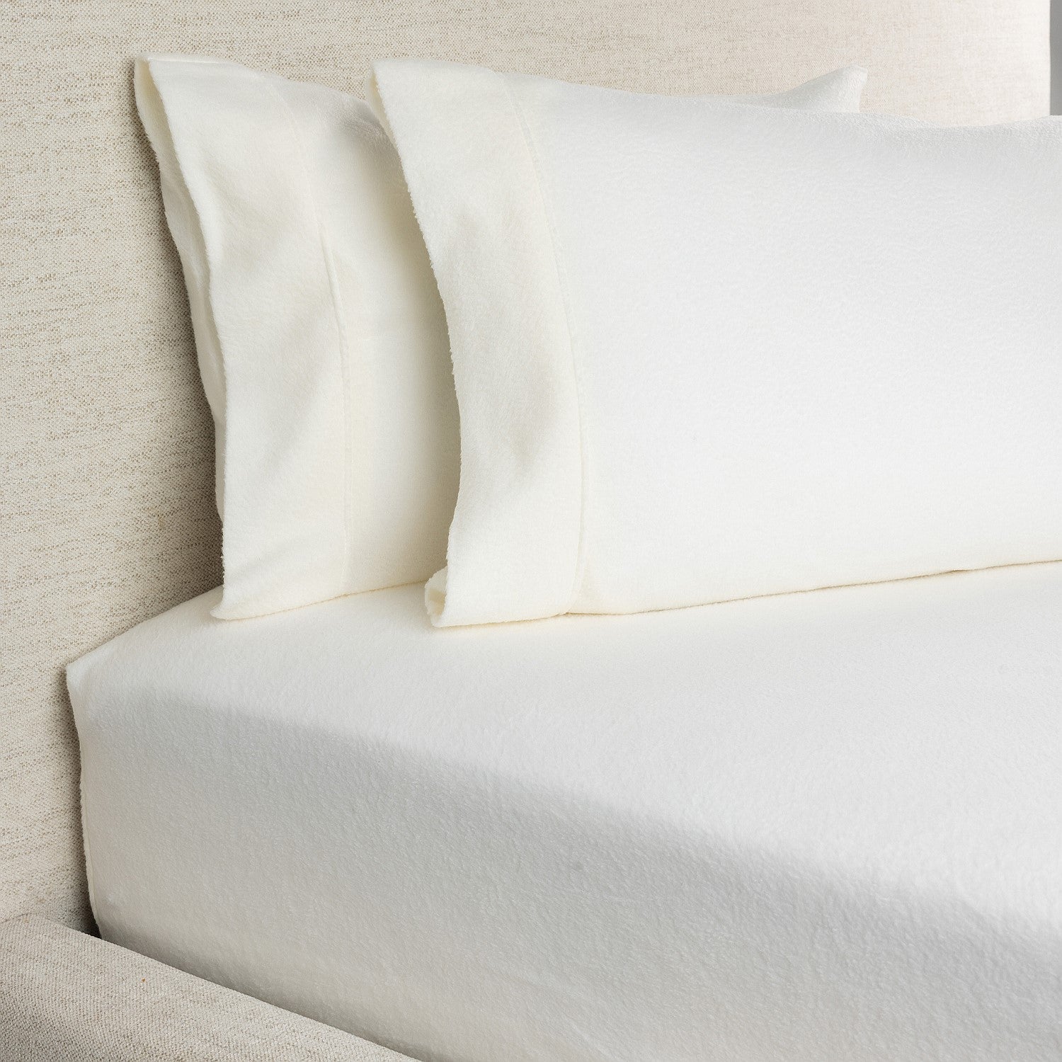 Close-up of a bed with white bedding and pillows against a neutral headboard.
