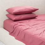 Pink bed sheets and pillows on a bed against a light wall.