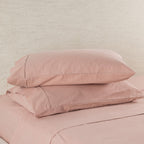 Two pink pillows on a matching pink bedspread against a beige wall.