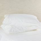 White pillowcases on a bed with a neutral headboard