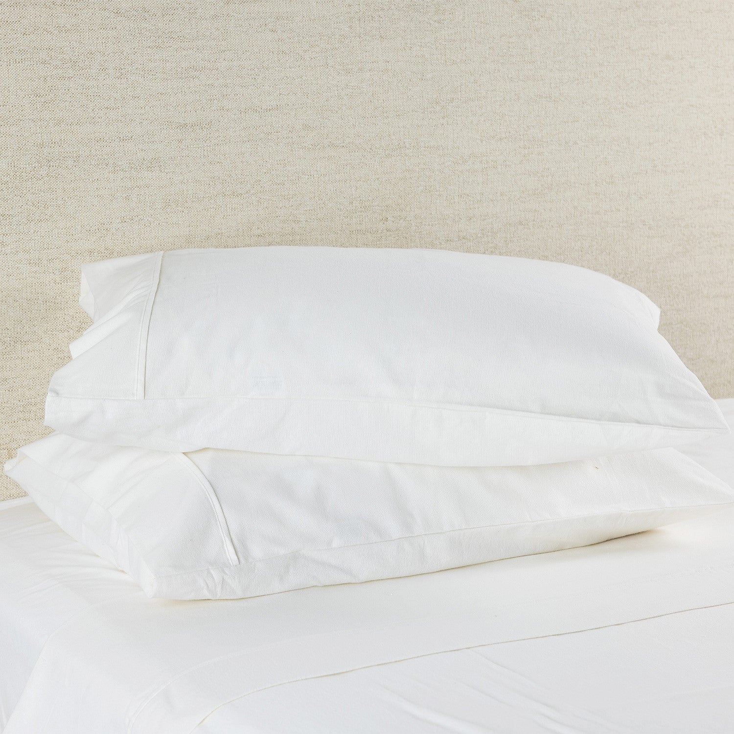 White pillowcases on a bed with a neutral headboard