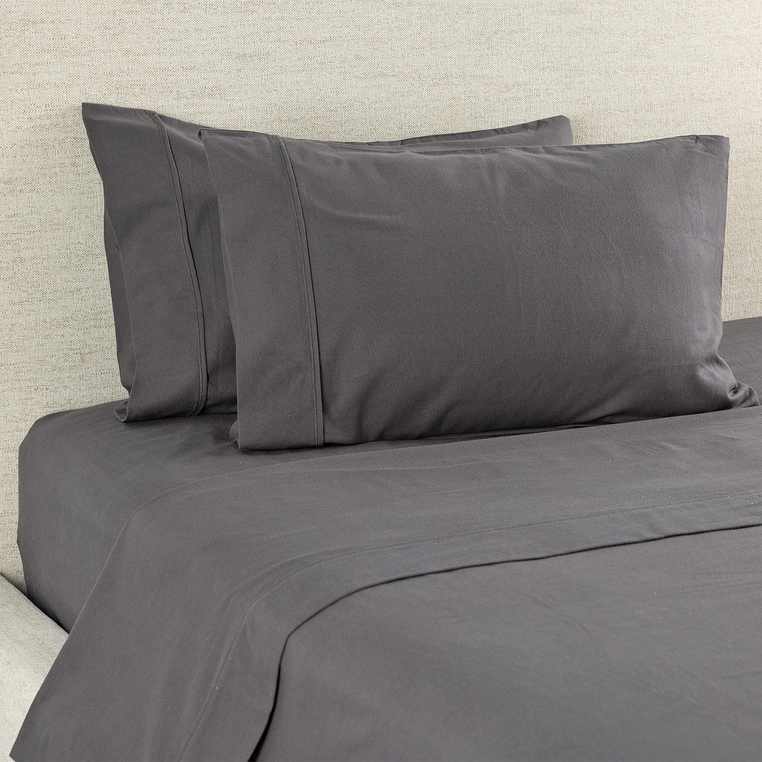 Gray bedding set with two pillows on a bed against a neutral wall.