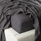 Dark gray fitted sheet on a bed with a pillow and blanket.