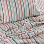 Striped bedding with pink, green, and blue colors on a bed.