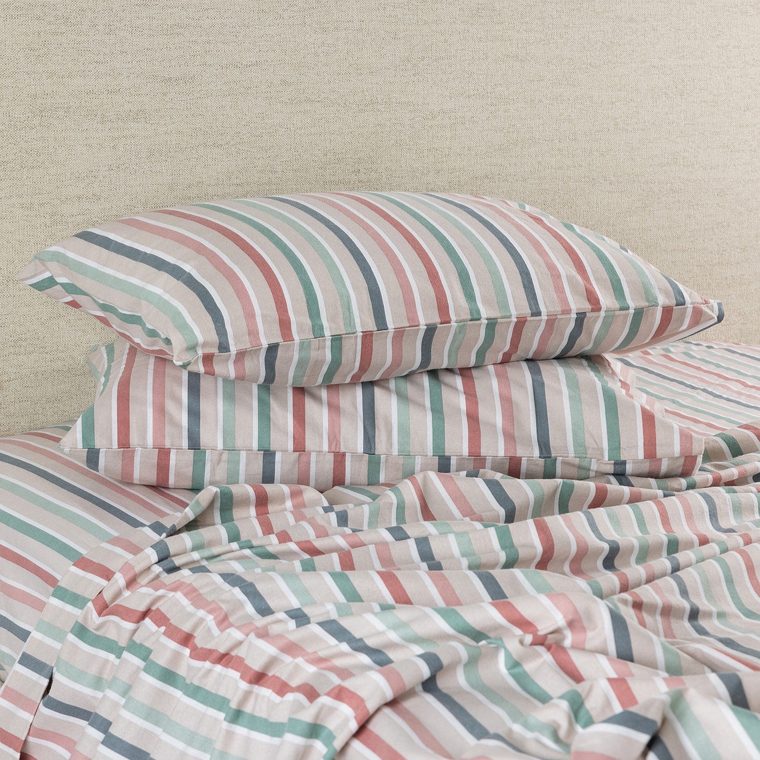Striped bedding set with pillows on a bed against a beige wall.