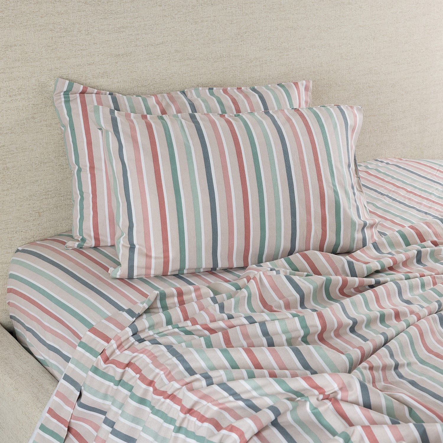 Striped bedding set with pillows on a bed against a beige wall.