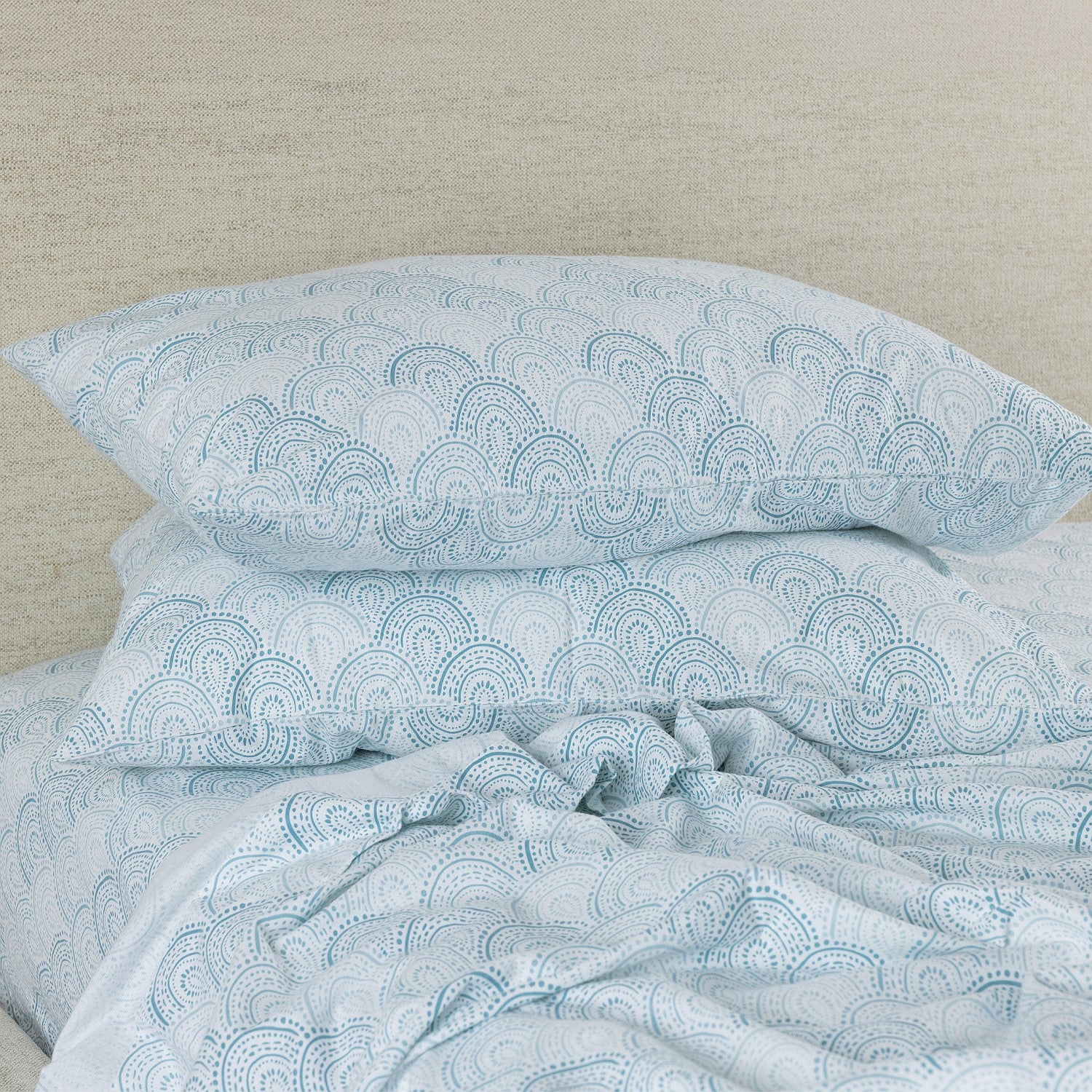 Teal patterned pillowcases on a bed with a neutral headboard.