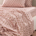 Close-up of the Marlo Mia Flat Sheet draped across a bed, showcasing the soft pink colour and repeating floral motif design.