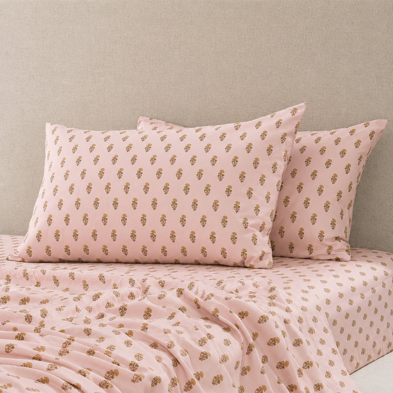 Pair of blush pink pillowcases with a delicate floral sprig print styled on a matching fitted sheet, with coordinating bedding draped across the bed.