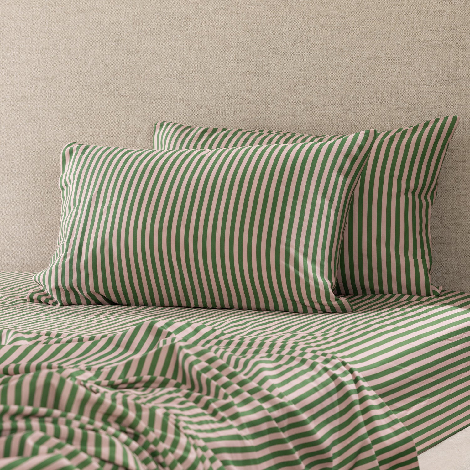 Two Marlo Mia green and blush stripe pillowcases styled on a bed with matching striped fitted sheet and coordinating bedding.